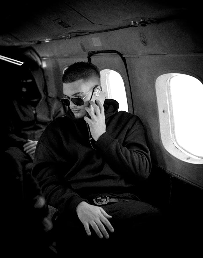 Black and white image of a man using a smartphone inside an airplane cabin for communication.